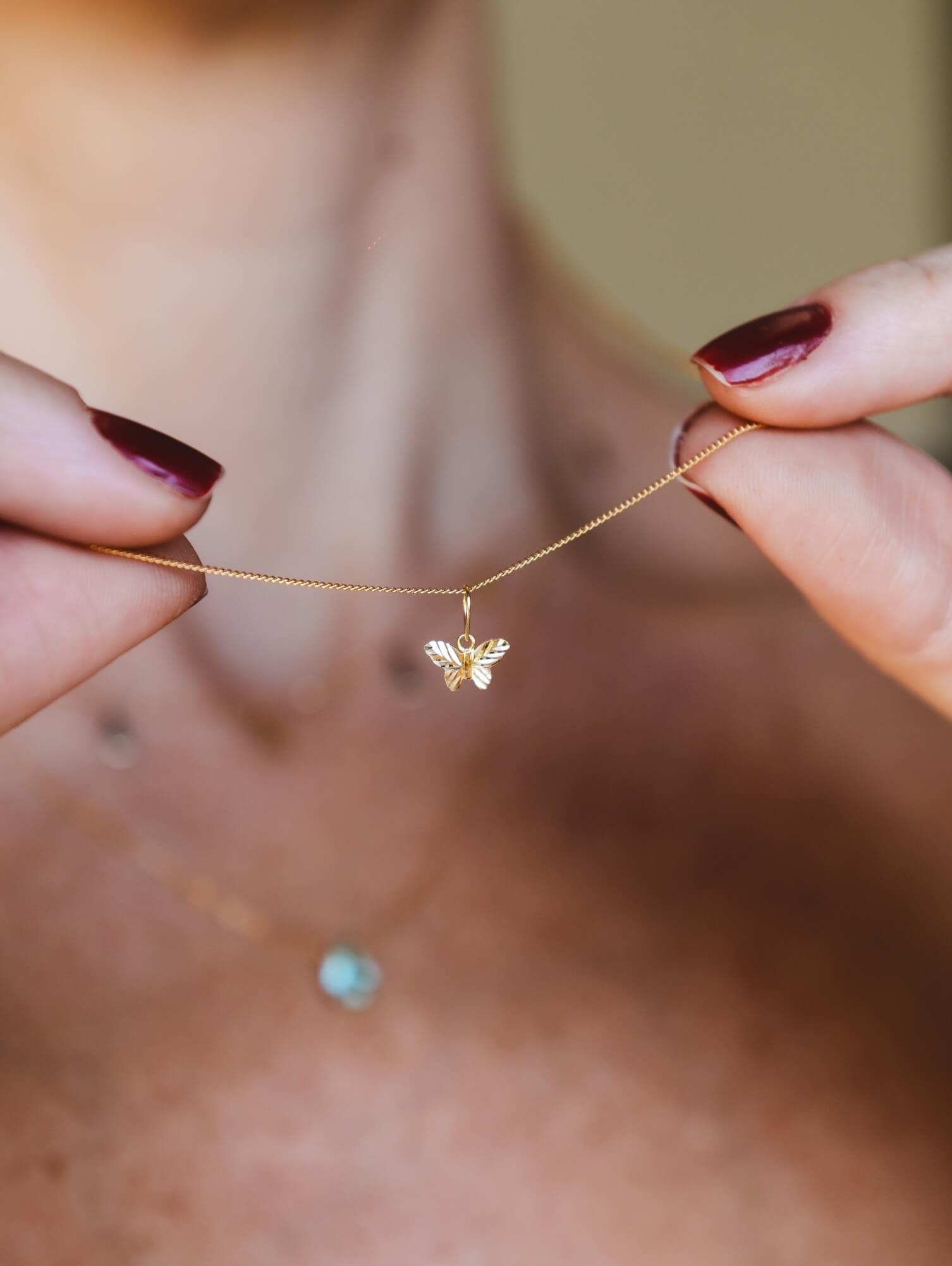 Pingente mini borboleta em ouro 18k exibido em uma corrente delicada.